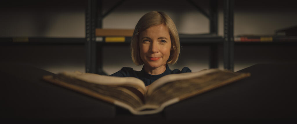 Lucy Worsley examining a large book.